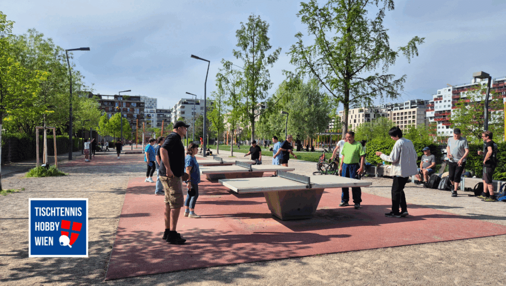 Viele Menschen spielen gleichzeitig Tischtennis im Freien - das Bild zeigt, wie der Sport Menschen unterschiedlichen Alters und Herkunft miteinander verbindet.