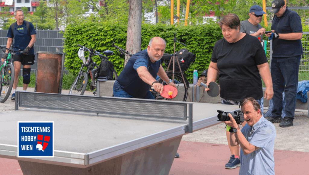 Menschen verschiedener Altersgruppen und Hintergründe spielen und interagieren rund um eine Tischtennisplatte in Wien - ein Ort gelebter Vielfalt und Begegnung.