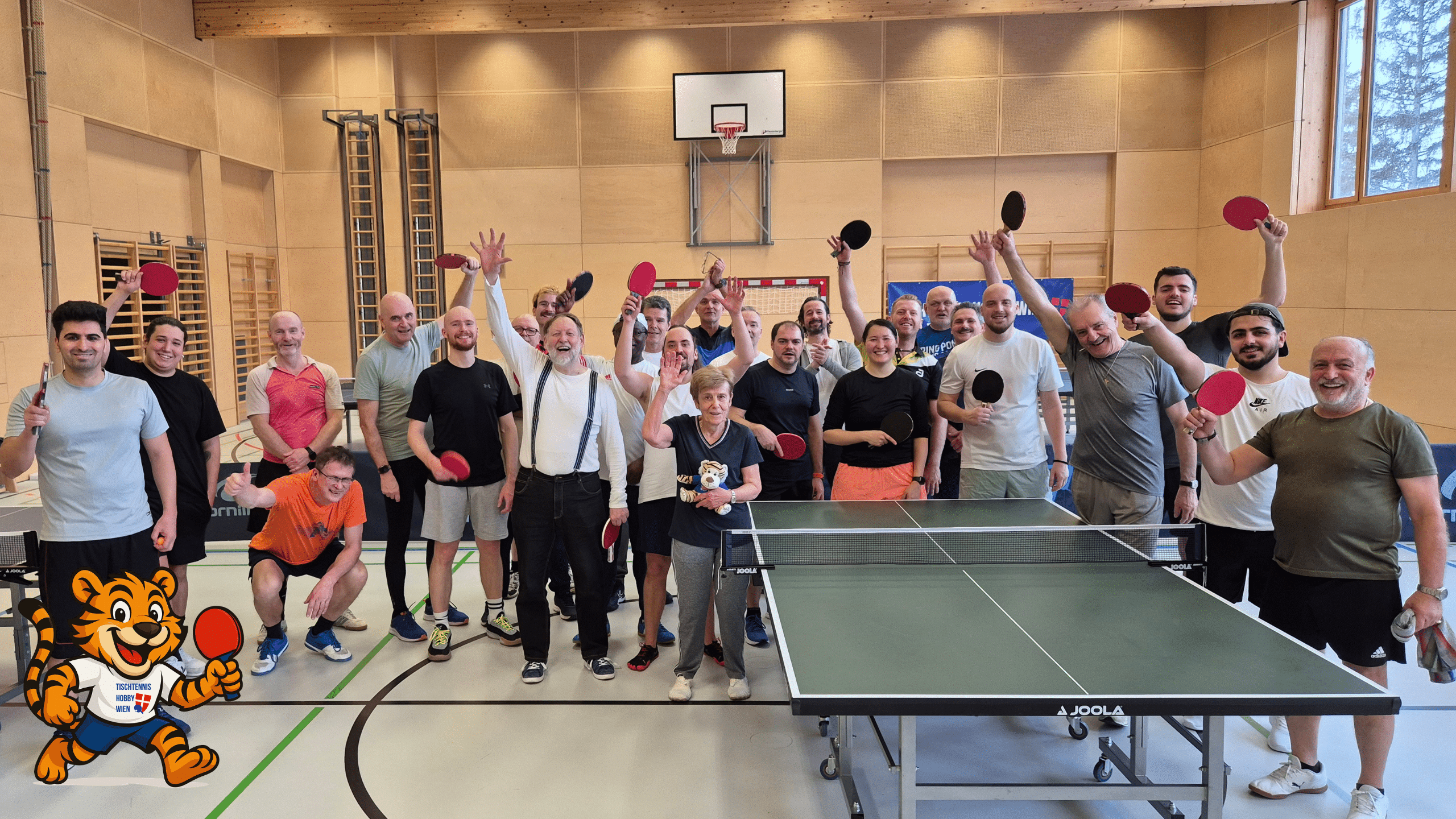 Zahlreiche begeisterte Teilnehmer:innen stehen mit Schlägern an den Platten, während das Maskottchen, der Ping Pong Tiger, inmitten der sportlichen Kulisse für gute Stimmung sorgt.