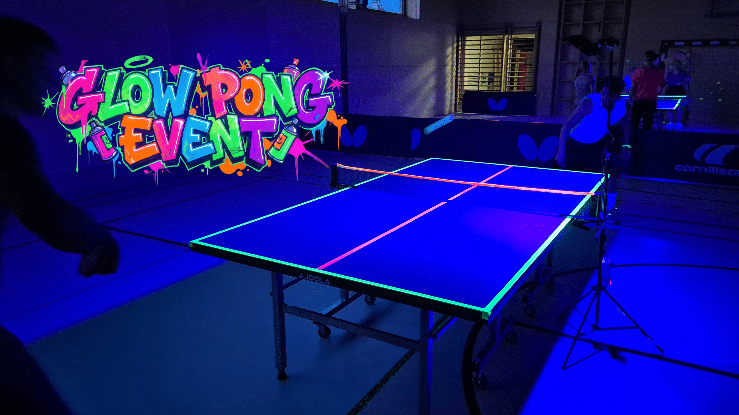 Leuchtendes UV Ping Pong Event bei Tischtennis Hobby Wien: Teilnehmer:innen spielen Tischtennis bei Schwarzlicht in einer dunklen Halle mit neon-leuchtenden Bällen und Markierungen für ein einzigartiges Sporterlebnis.